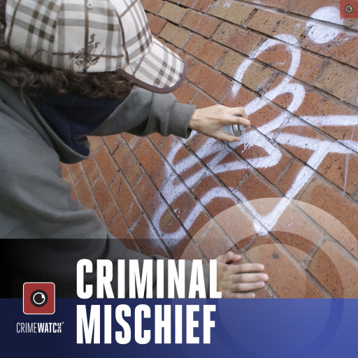 A young man spray painting graffiti on a brick wall.